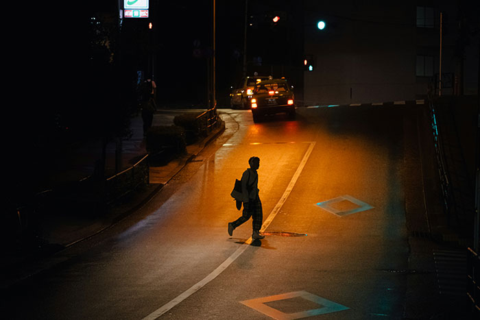 Security guard reviews weird camera footage of a person crossing a dimly lit street at night near a parked taxi.