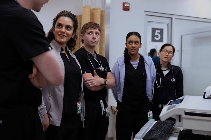 A group of insufferable Pitt fans in medical scrubs in a hospital hallway discussing season 2 additions and romance.
