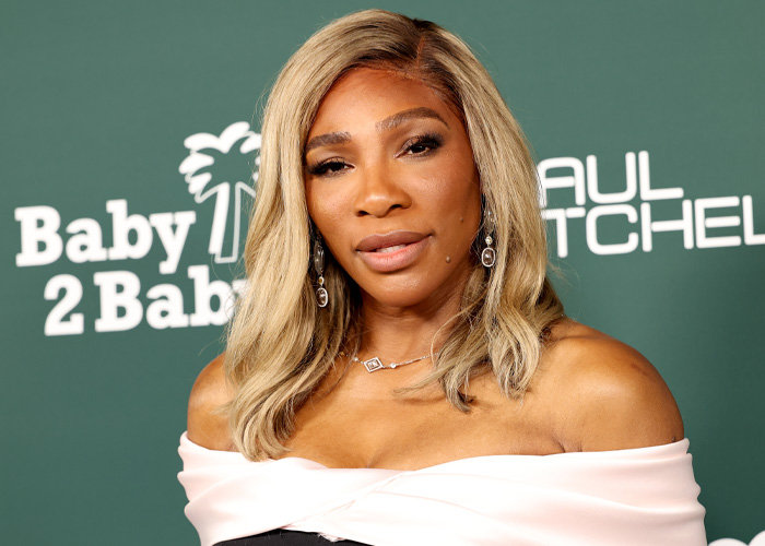 Serena Williams posing at an event with blond hair and elegant earrings, capturing the viral knees are kneeing moment.