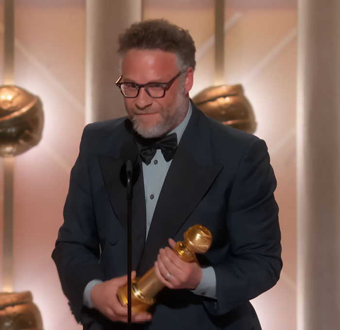 Seth Rogen holding a Golden Globe award on stage at the ceremony following Pamela Anderson's call for an apology.