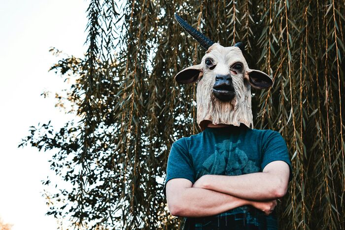 Person wearing a realistic goat mask standing with arms crossed outdoors, illustrating weird and shocking public behavior.