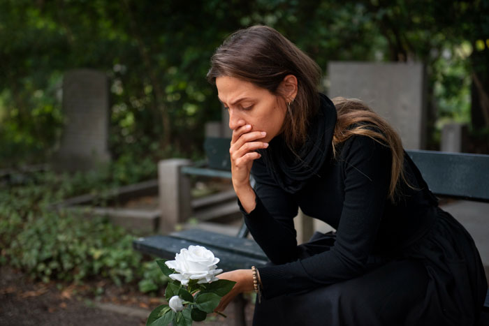 Woman grieving on bench holding white rose, reflecting SIL turning her back during her time of need.