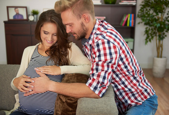 Pregnant couple smiling and bonding on the couch, highlighting family love and support during important moments.