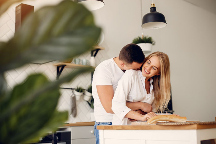 Happy couple embracing in a modern kitchen, illustrating a rich man realizing his helping hand is bankrolling his sister's jobless boyfriend. Happy couple embracing in a modern kitchen, illustrating a rich man realizing his helping hand is bankrolling his sister's jobless boyfriend.