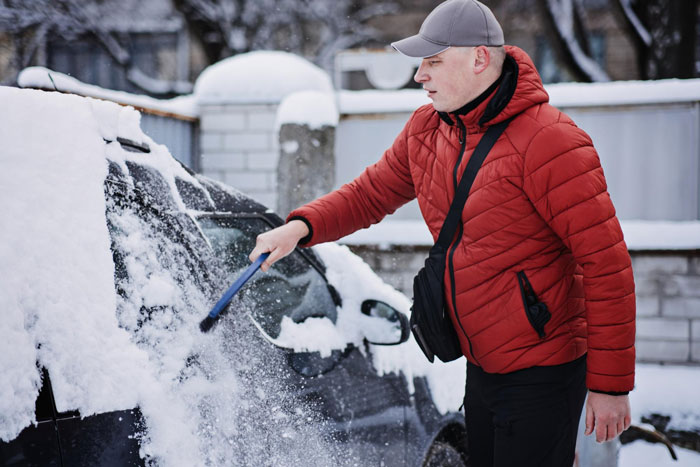 Man in red jacket snowing neighbours illegally parked car on a residential street during winter snowfall. Man in red jacket snowing neighbours illegally parked car on a residential street during winter snowfall.