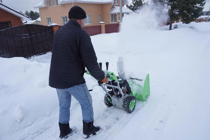 Man using a snowblower to clear snow in a driveway near a neighbours illegally parked car during winter. Man using a snowblower to clear snow in a driveway near a neighbours illegally parked car during winter.
