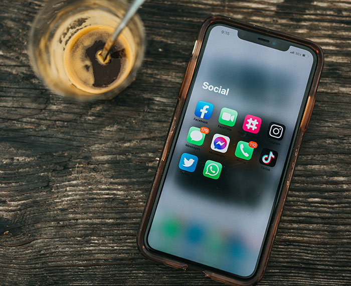 Smartphone displaying social media apps on wooden table with a glass of coffee, related to Barron Trump emergency call.