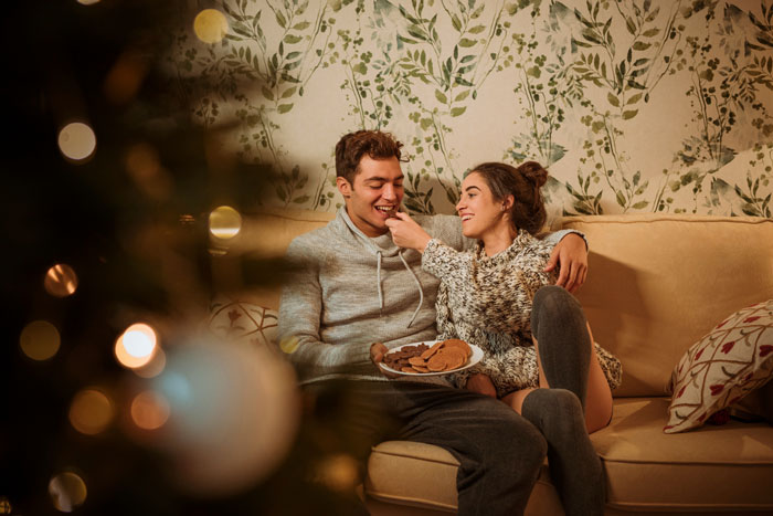 Young couple sharing cookies on a couch, illustrating a son and girlfriend relationship after high school advice conflict. Young couple sharing cookies on a couch, illustrating a son and girlfriend relationship after high school advice conflict.