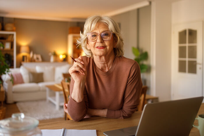 Older woman smiling thoughtfully at home, symbolizing mom inviting son's girlfriend to dad's party and his surprised reaction.