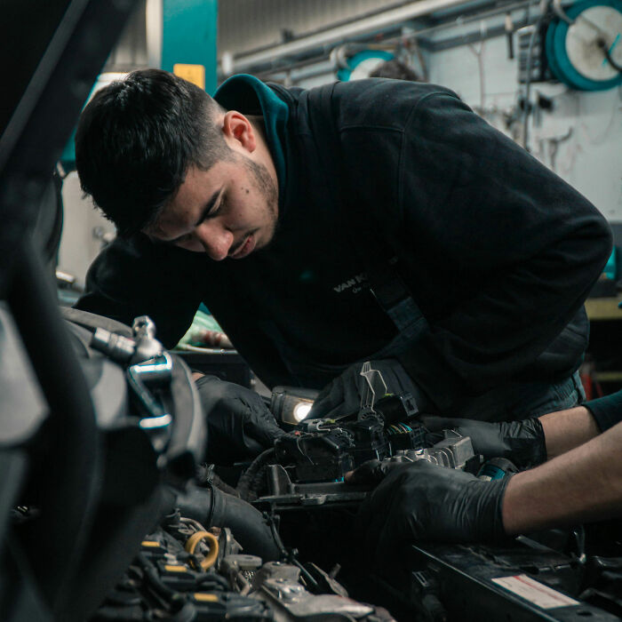Mechanic intensely working on a car engine, highlighting coworker stories about unhinged behavior at the workplace.