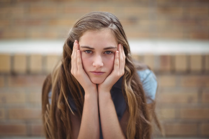 Teenage girl with long hair resting her face in hands, appearing thoughtful in a setting related to step-daughter trust fund.