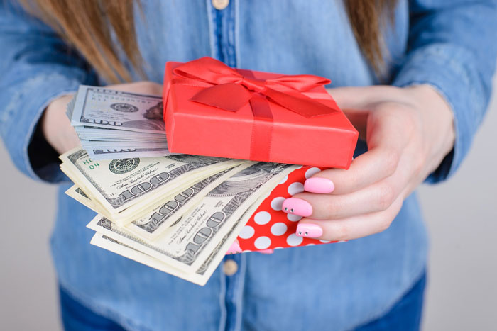 Woman holding a red gift box filled with cash representing a step-daughter trust fund concept.