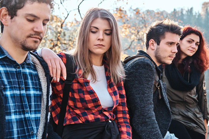 A step-kids mom looking upset and distant while standing outdoors with three young adults during autumn.