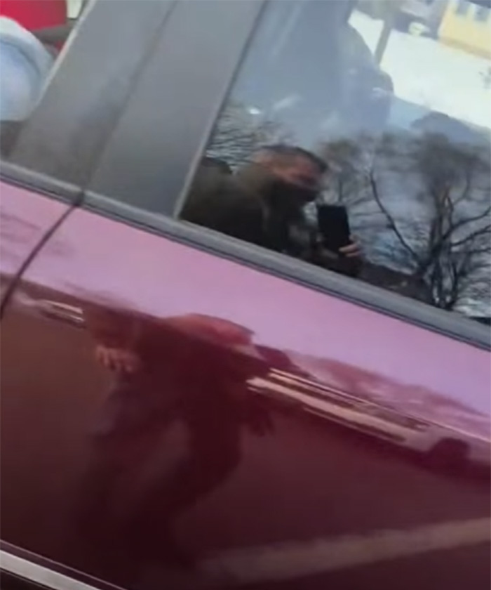 Reflection of a person holding a phone visible in car window, related to Stephen King facing backlash over ICE agent post.