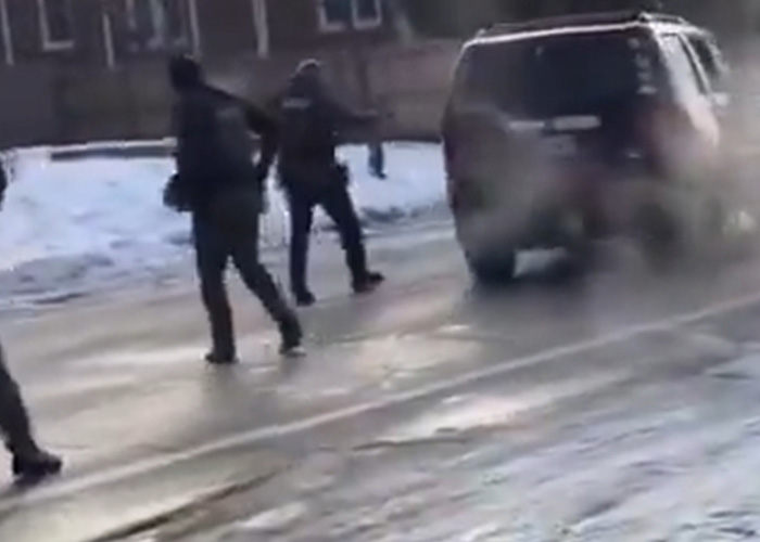 ICE agents in tactical gear walking near a vehicle on a snowy street amid tense law enforcement activity.