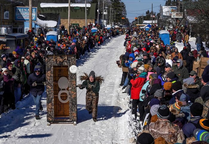 Crowd watches a quirky winter race featuring people running with decorated outhouse in a strange tradition event outdoors.