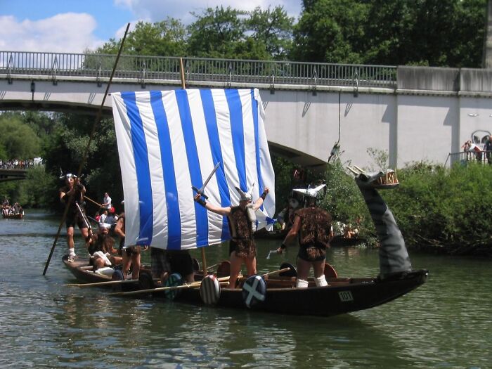 A group dressed in Viking costumes on a boat with a striped sail during strange traditions from around the world.