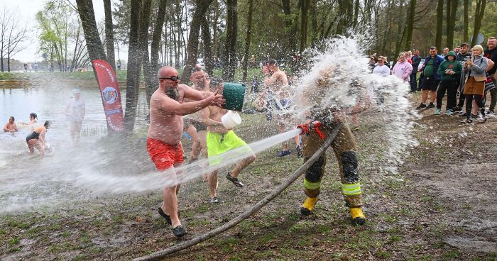 Men participating in a strange water fight tradition in a park, with spectators watching and cheering around them.