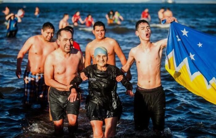 Group of people participating in a strange tradition, swimming in cold water, one holding a colorful flag celebrating unusual world customs.