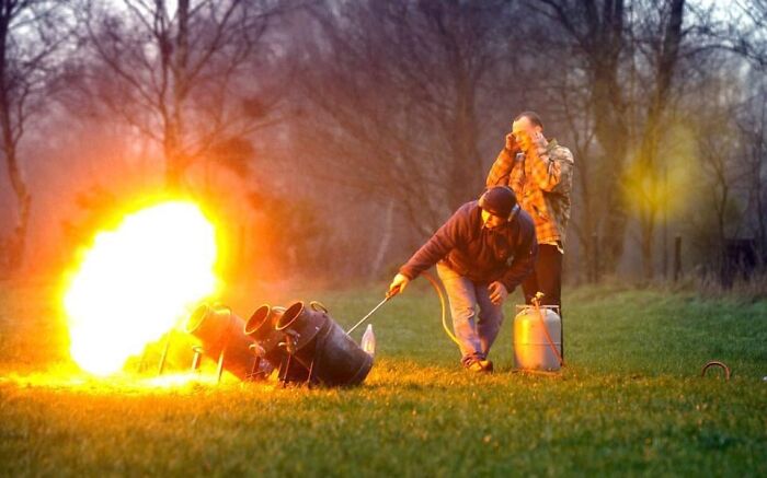 Two men lighting a large flame from cannons outdoors, illustrating strange traditions from around the world.