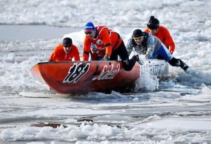 Four people in orange and blue racing a canoe through icy waters, showcasing strange traditions from around the world.