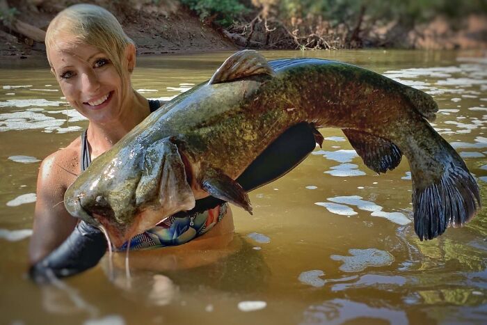 Woman holding a large fish in muddy water, illustrating strange traditions from around the world with unusual catches.
