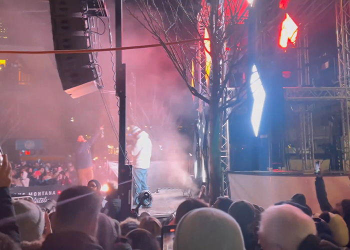 Crowd gathered at night with smoke and bright lights, capturing the scene related to ski resort explosion survivors.