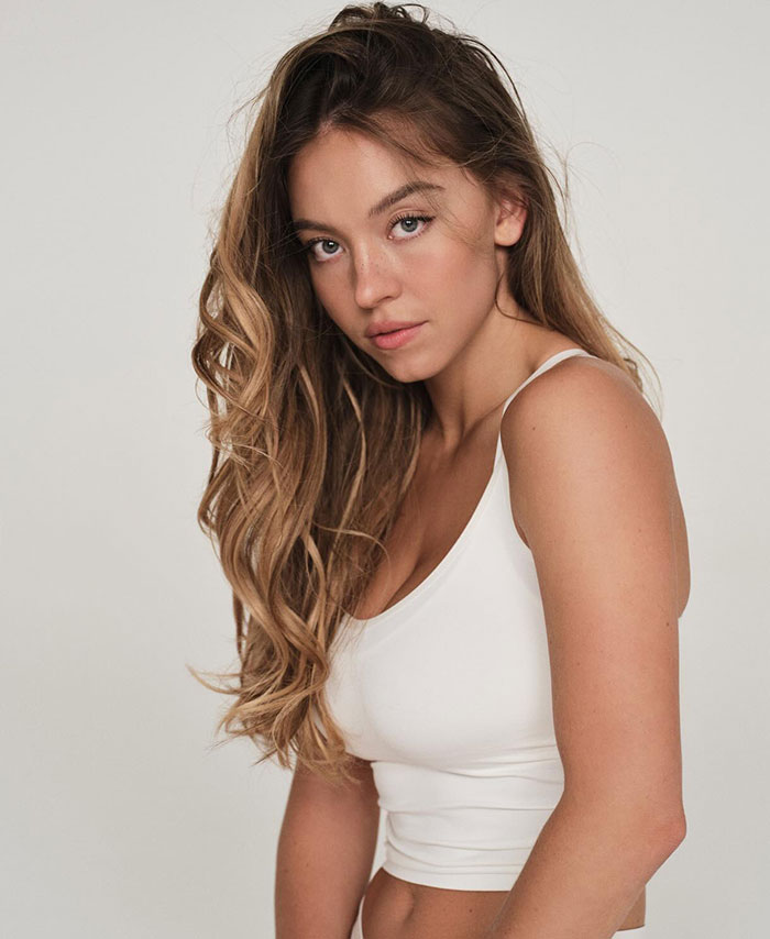 Sydney Sweeney posing in a white top, promoting her new racy lingerie line with a confident and alluring look.