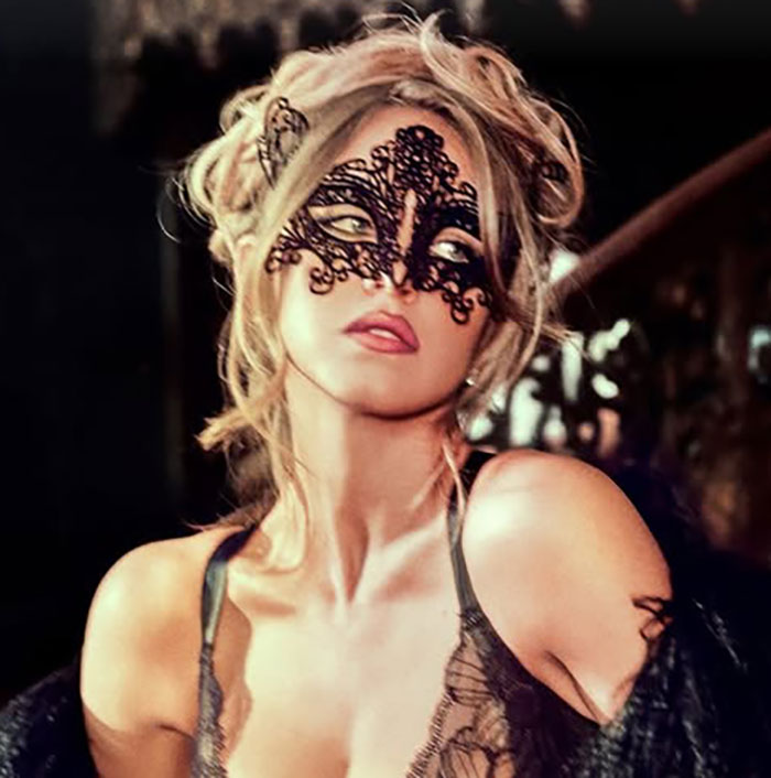 Sydney Sweeney wearing intricate black lace lingerie and matching lace mask in a dimly lit, elegant setting.