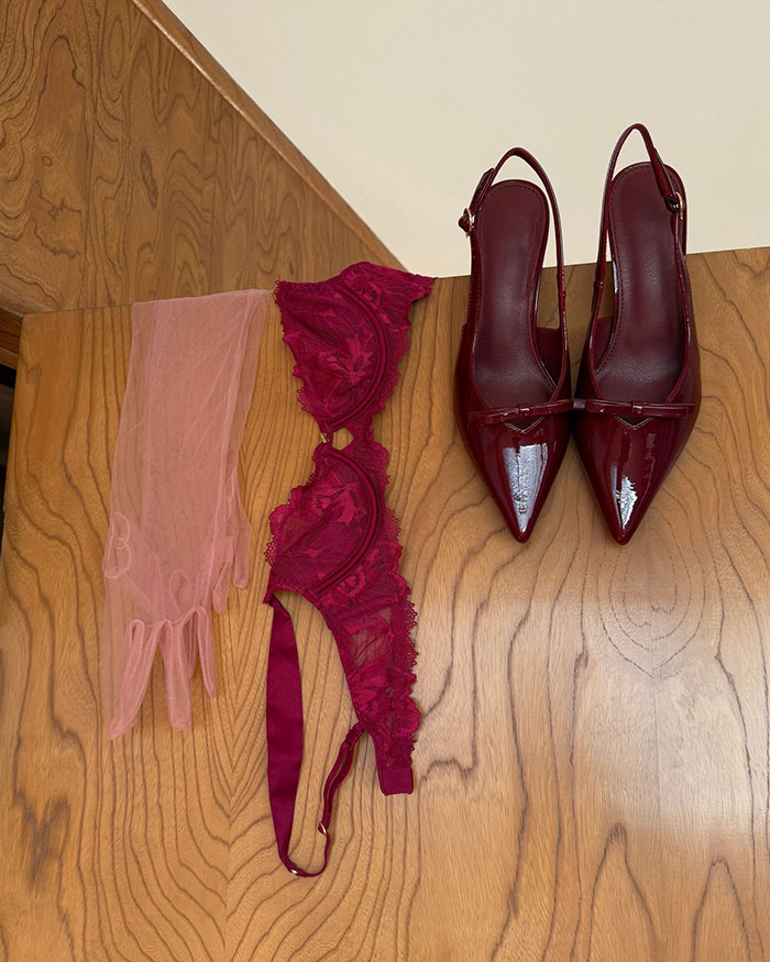 Sheer pink gloves, red lace lingerie, and matching red patent leather heels laid out on a wooden surface.