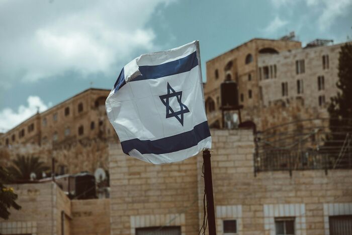 Israeli flag waving in front of historic buildings, illustrating things normal in their country but offensive elsewhere.