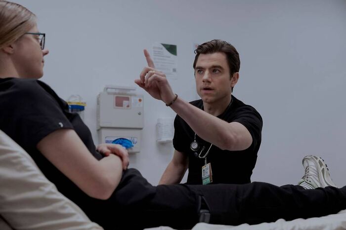 Male medical professional wearing black scrubs talks to patient in clinical setting illustrating disorder in medical drama. Male medical professional wearing black scrubs talks to patient in clinical setting illustrating disorder in medical drama.
