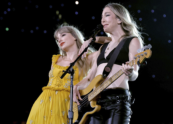 Taylor Swift in a yellow dress performing on stage with a bassist, fans scrutinizing her wedding look choices