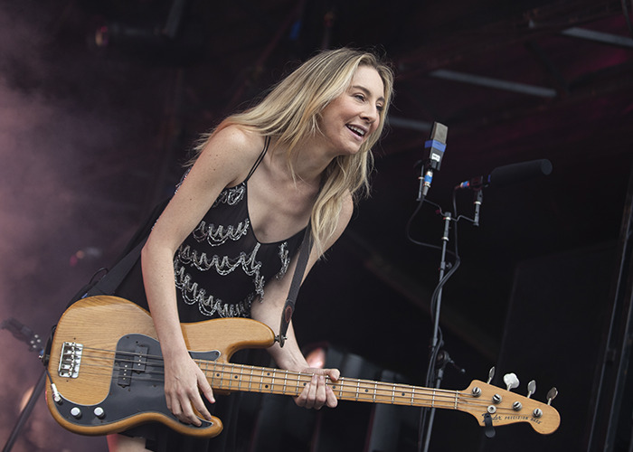 Female musician playing bass guitar on stage, capturing Taylor Swift's wedding look scrutinized by fans in a live performance.