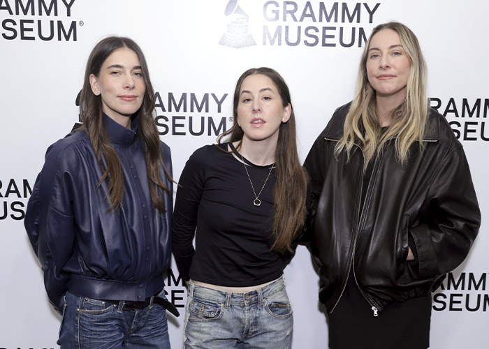 Three women posing at the Grammy Museum event, with fans scrutinizing Taylor Swift's wedding look for upstaging concerns.