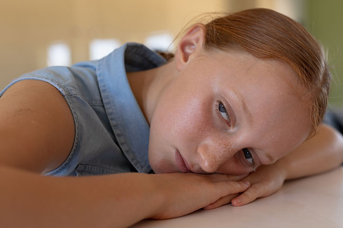 Young girl with red hair resting her head on her arms, looking sad and ignored during an emergency situation.