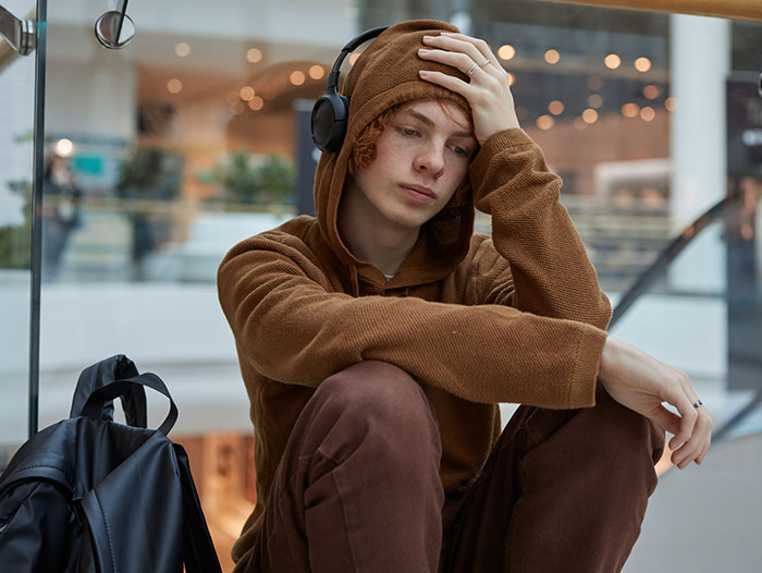 Teen still hurt sitting wearing headphones and brown hoodie, reflecting on abandonment and emotional pain six years later.