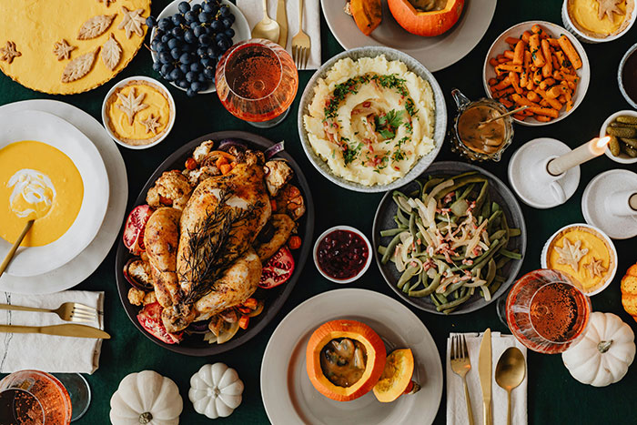 Thanksgiving dinner spread with turkey, mashed potatoes, green beans, and autumn decor on a dark tablecloth.