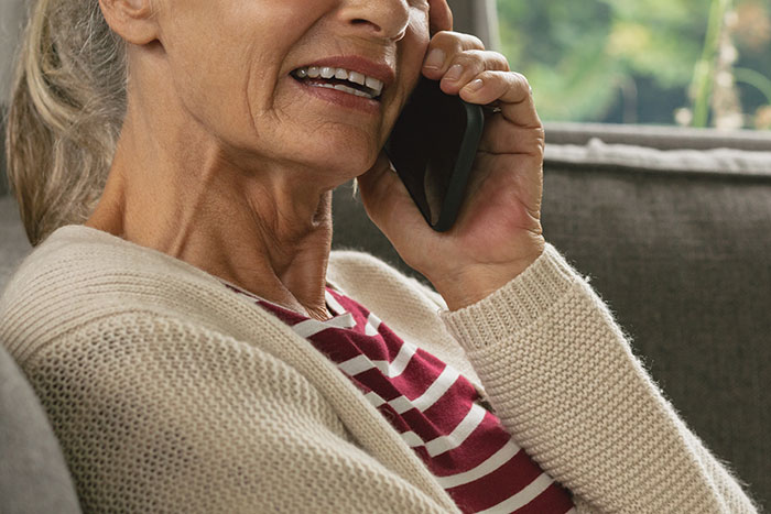 Woman refusing to attend Thanksgiving, talking on phone with serious expression, sitting on a couch indoors.