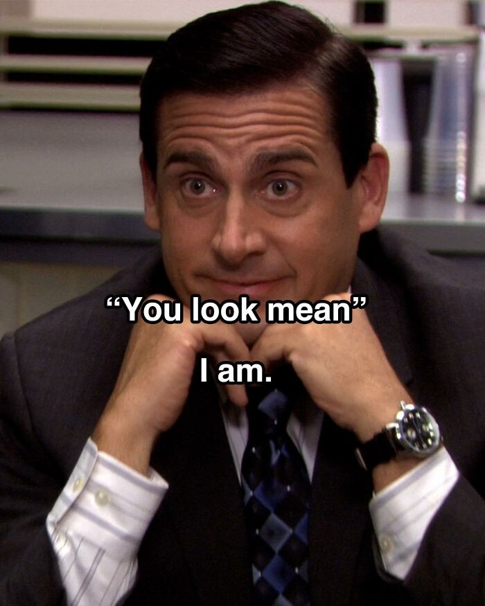 Michael Scott from The Office in a suit, resting his chin on hands with a funny meme about looking mean.