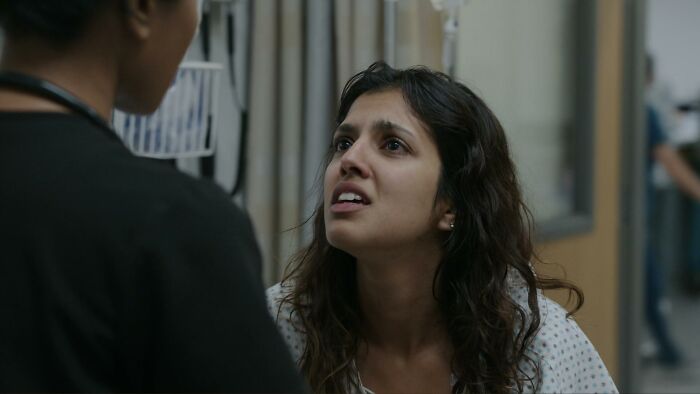 Patient in hospital gown speaking with medical professional in a hallway, depicting realistic medical cases at The Pitt.