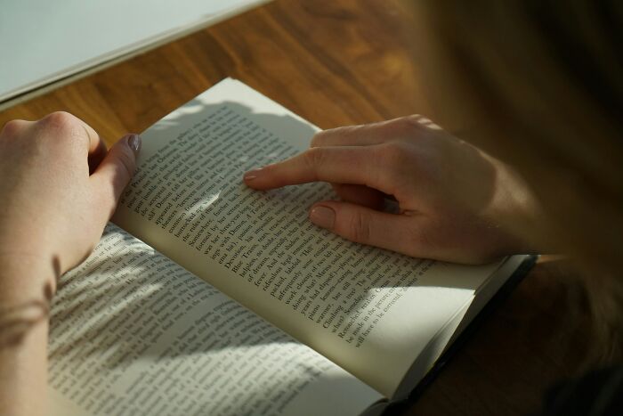 Person using finger to follow text in an open book, illustrating cheat codes for making everyday life easier.