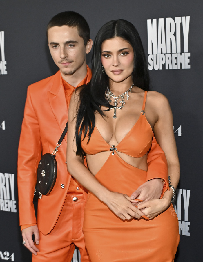 Timoth&eacute;e Chalamet and Kylie Jenner posing together at a Marty Supreme event, both wearing orange outfits.