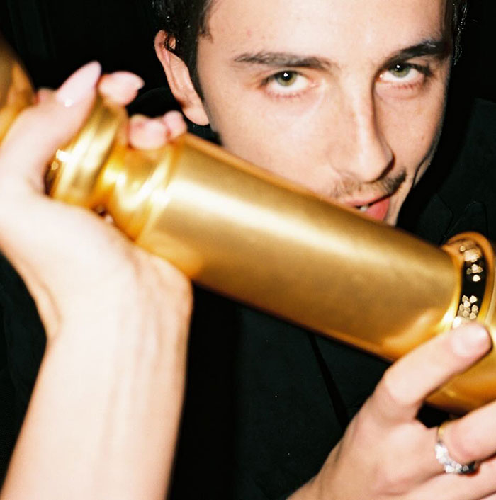 Timoth&eacute;e Chalamet holding a golden object close to his face in a dimly lit setting, sparking backlash online.