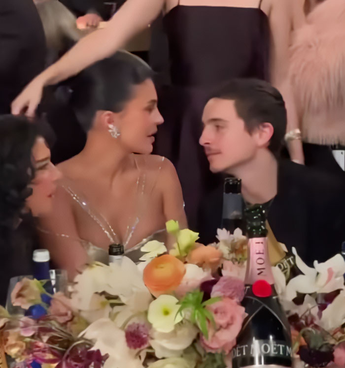 Timoth&eacute;e Chalamet and Kylie Jenner seated at a floral-decorated table during a formal event with drinks nearby.