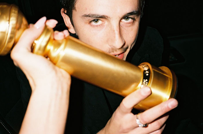 Timoth&eacute;e Chalamet holding a Golden Globe award close to his face in a dimly lit setting after fight news.