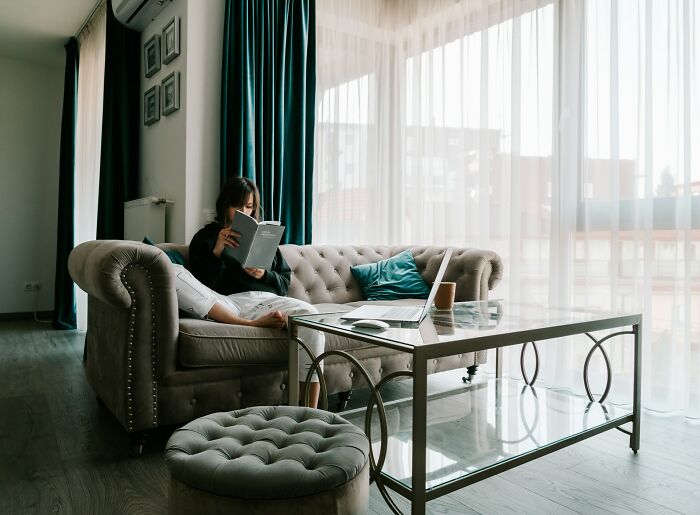 Woman relaxing on a sofa reading a book in a bright living room, illustrating things women do to feel safer living alone.