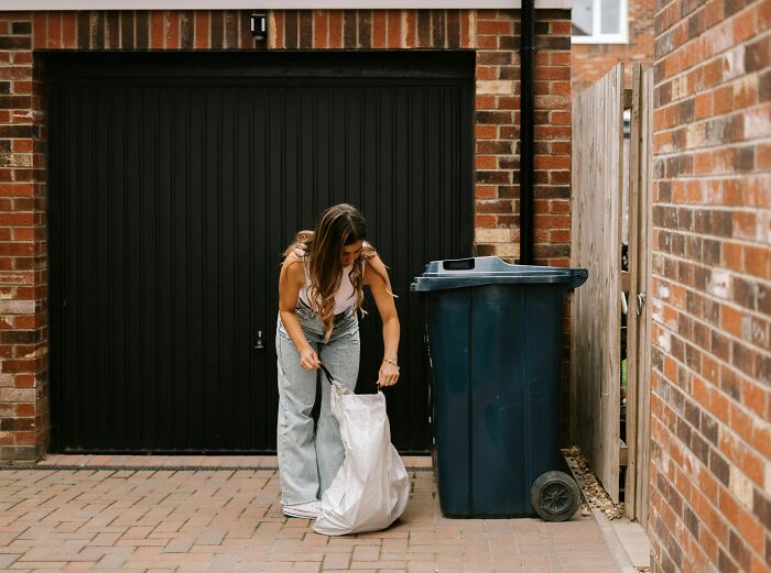 Woman outside home taking out trash next to a bin, illustrating petty fights couples had over the Christmas period.