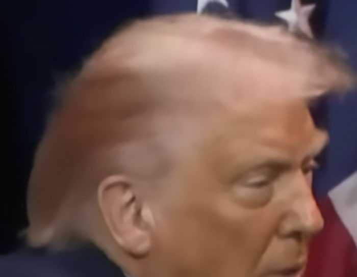 Close-up profile of a man with pink-tinted hair and an American flag in the background, highlighting hair color change.