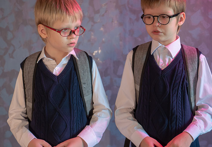 Twin boys in matching school uniforms and glasses, illustrating parent refuses to make twins less similar for school. Twin boys in matching school uniforms and glasses, illustrating parent refuses to make twins less similar for school.
